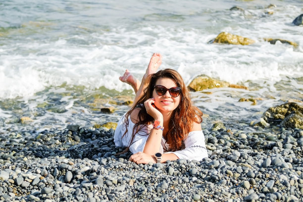 一个漂亮的红头发女孩躺在海滩的石头上。度假胜地的性感女人图片下载