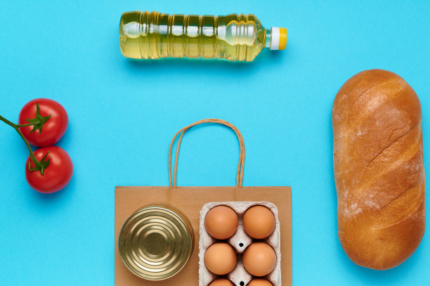 顶视图,flatlay。一套产品与纸袋在蓝色背景。从商店买的食物。葵花籽油，鸡蛋，新鲜番茄和面包。交付和捐赠概念图片下载