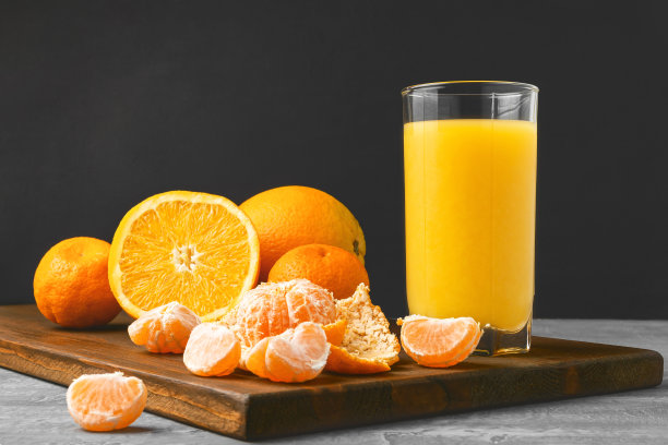 一杯新鲜的橙汁，整个和切片水果在木板上的深色背景与复印空间图片下载