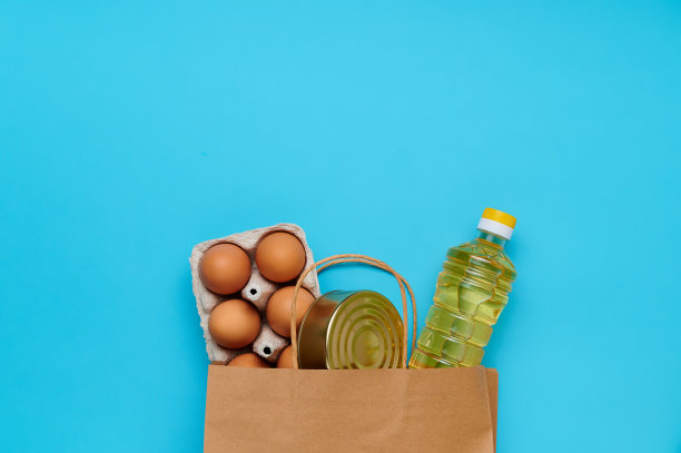 顶视图,flatlay。套内产品纸袋上的蓝色背景。包装商店里的食物。葵花籽油、鸡蛋、罐头食品。交付和捐赠的概念图片下载