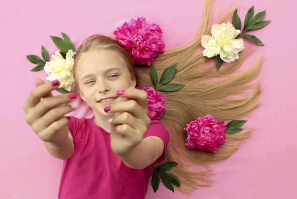 一个拿着牡丹花的女孩，一头漂亮的金发，戴着五颜六色的儿童指甲图片下载
