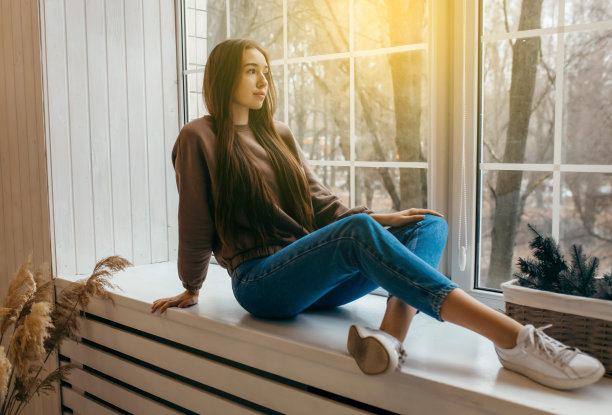 穿着帽衫的年轻女子坐在窗台上摆姿势图片下载