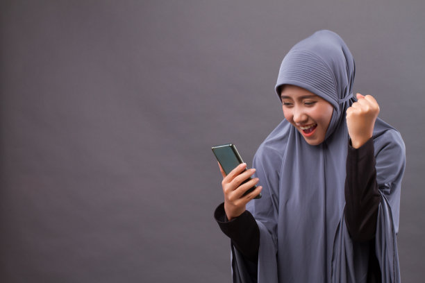 兴奋，快乐的穆斯林妇女使用智能手机，无线互联网设备图片下载