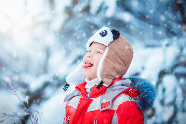 快乐快乐的男孩在冬天的公园里用嘴巴捕捉雪花，享受冬天。有选择性的重点图片下载