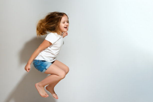 快乐的小女孩在跳。灰色背景上穿着短裤和t恤的孩子。图片下载