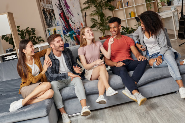 快乐的时刻。年轻漂亮的女孩告诉她最好的朋友一些事情，让他们一起坐在家里的沙发上大笑。快乐的多元文化的人们一起在室内放松图片下载