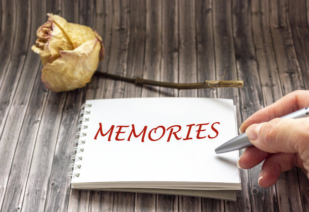 木桌上放着一朵发黄的老玫瑰。女人的手把回忆写在笔记本上。图片下载