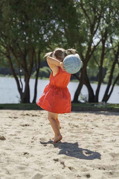 可爱的小女孩穿着红色的裙子在沙滩上玩球图片下载