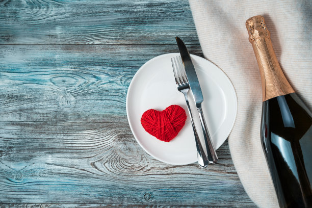 毛衣上放着香槟，木制背景上放着心形盘子和餐具。图片下载