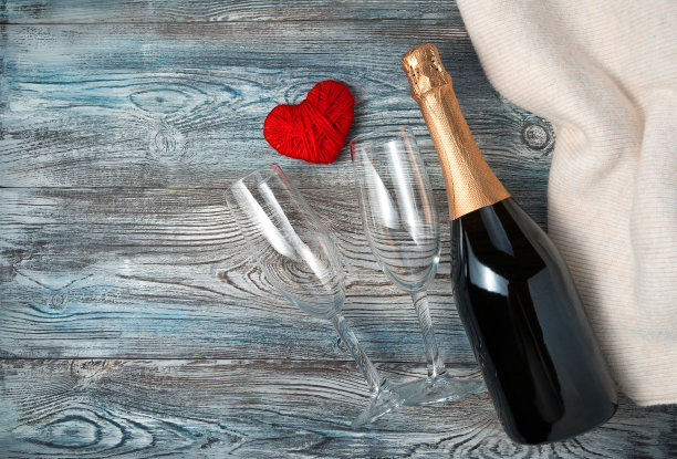一瓶香槟，两个杯子，木背景上的一颗爱心和一件毛衣。图片下载