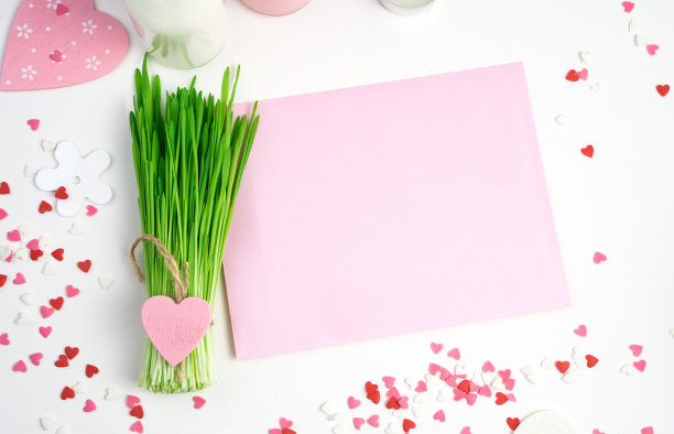 浪漫的背景粉红色色调的心，粉红色的信封和绿色的花束在一个浅色的背景图片下载