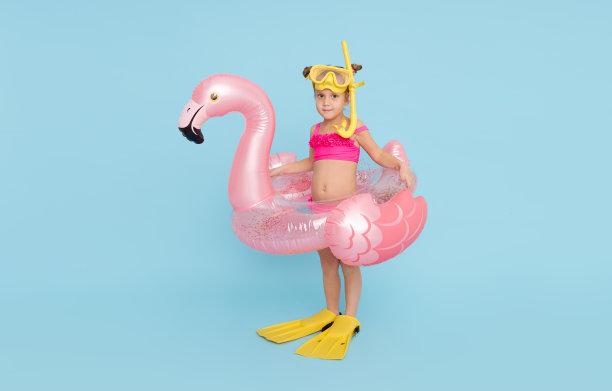 一个穿着泳衣、戴着潜水面罩、脚蹼、戴着充气戒指的快乐女孩要去度暑假了。蓝色背景图片下载