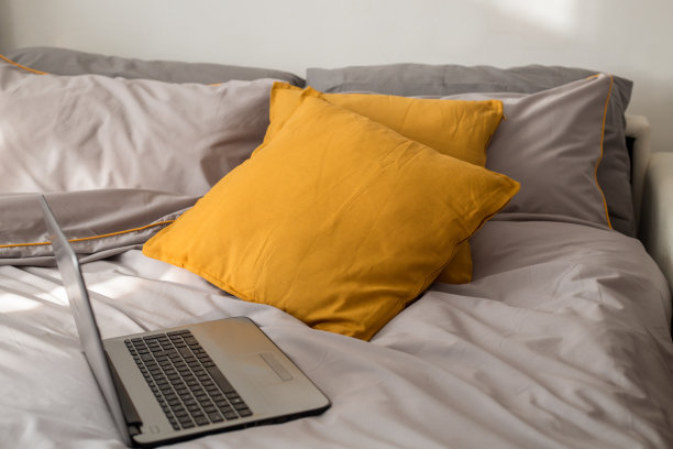 卧室，工作场所在流行的床与笔记本电脑和发光的黄灰色枕头新潮的颜色2021室内设计图片下载
