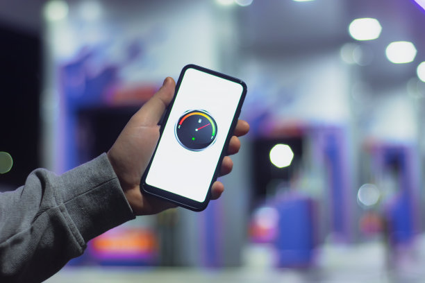 在一个夜间加油站的背景下，一名男子拿着一部智能手机，屏幕上显示着一个数字油表。图片下载