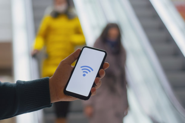 超市免费上网。一名男子手持智能手机模型，白色屏幕上有一个图标，背景是自动扶梯和商场里的人群。图片下载