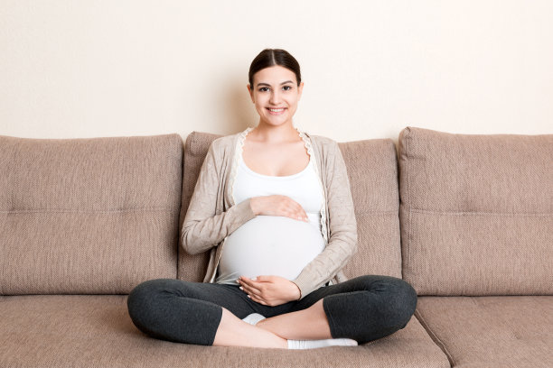 可爱的白人未来妈妈躺在明亮的客厅沙发上，手放在肚子上的照片图片下载