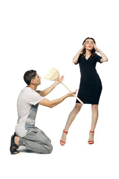 一个穿着家装的男人跪着向一个穿着晚礼服的漂亮女人举起扫帚，她轻蔑地击退了他。孤立在白色背景上图片下载