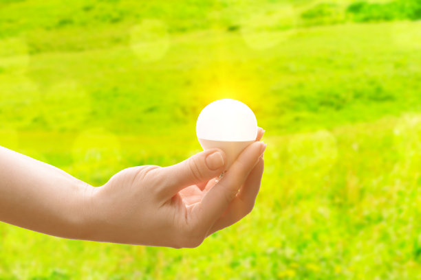 生态和太阳能的自然能源概念，手与一个发光的灯泡在一个绿色的背景图片下载