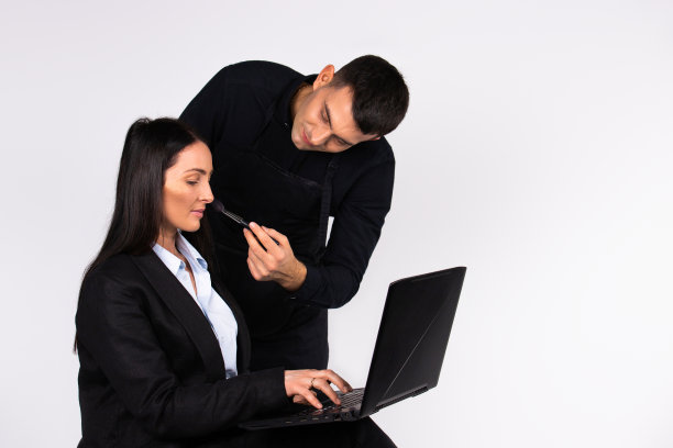 化妆师在白色背景上用笔记本电脑为商务女性化妆。图片下载