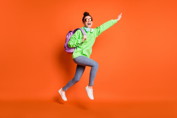 全长照片的粗心奔跑年轻女士穿着绿色运动衫背包孤立明亮的橙色背景图片下载