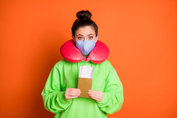 照片可爱甜美的年轻女士穿着绿色运动衫颈部枕头医疗面具票孤立明亮的橙色背景图片下载