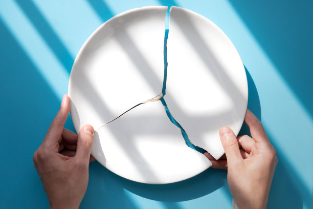 男人的手拿着一个破碎的白色盘子在蓝色的背景下，阳光。比喻离婚，关系，友谊，婚姻破裂图片下载