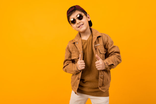 欧洲时尚少年在棕色牛仔夹克和时尚眼镜摆姿势与复印空间黄色背景图片下载