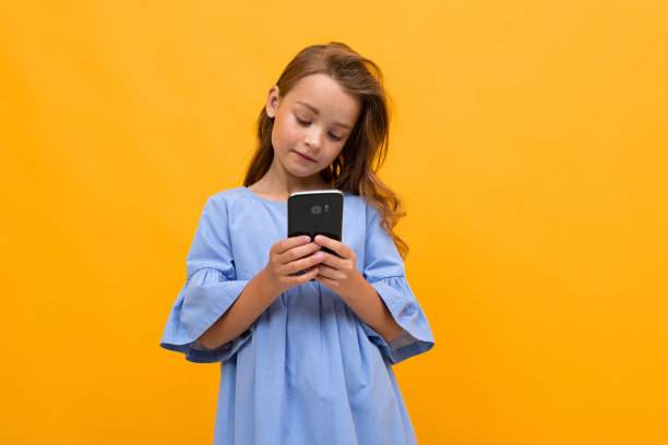 一个穿着裙子的十几岁女孩坐在互联网上，手机放在黄色的背景上，有复制空间图片下载