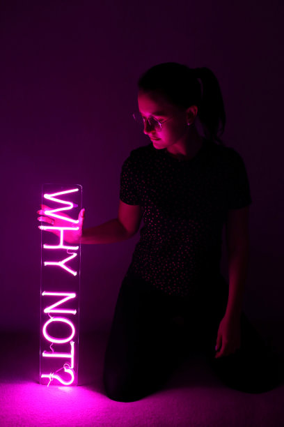 漂亮的年轻女孩拿着粉红色的霓虹灯，为什么不呢?时尚的风格。图片下载