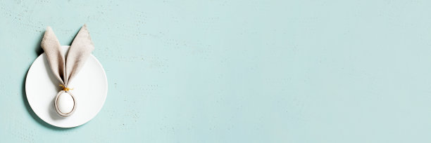 带复活节彩蛋装饰兔子耳朵的亚麻餐巾横幅放在蓝色纹理的桌子上图片下载