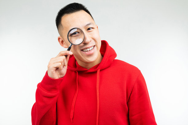 一名身穿红色毛衣的黑发男子正通过放大镜注视着一个孤立的白色背景图片下载