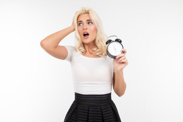 一个穿着白色t恤、满头白发的女孩，在一个孤立的白色背景下，手里拿着一个闹钟，担心自己会迟到图片下载