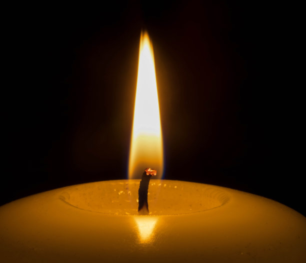 靠近白色的蜡烛火焰在黑暗的背景图片下载