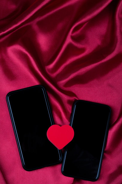 红心和两部手机在红绸布上随波浪起伏。网络约会，拷贝空间，情人节概念。图片下载