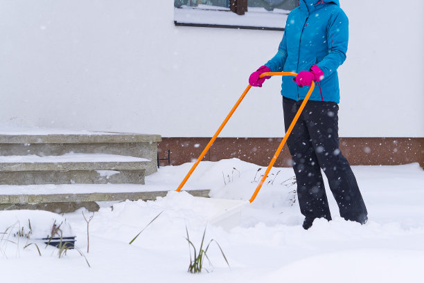 在冬天用铁锹清扫雪的妇女。在屋前的人行道上铲雪的女人图片下载