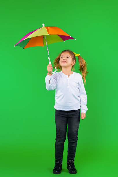 全身的照片。一个带着绿色背景的彩色伞微笑的孩子。图片下载