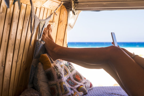 近距离的女人美丽的腿和人们放松在一辆面包车与海滩和海景夏季度假车辆-女性短信与现代电话连接在户外旅行图片下载
