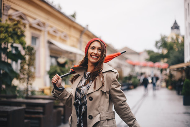 一个年轻的女孩，拿着她的橙色伞，走在城里。图片下载
