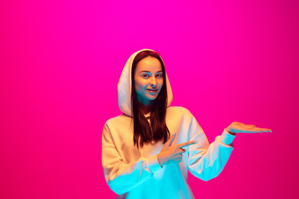 白种人美丽的女人的肖像孤立在粉红色的工作室背景在五颜六色的霓虹灯图片下载