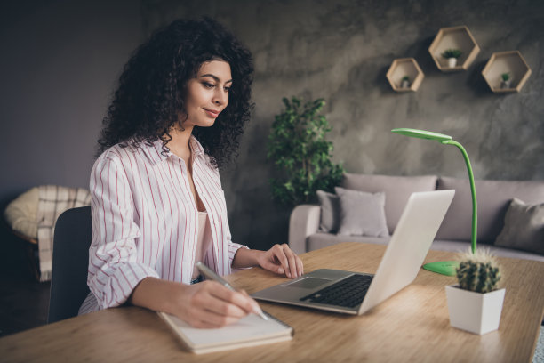 在工业办公室室内用笔记本电脑工作的女人在记事本上写东西的照片图片下载