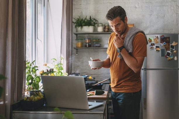 英俊的年轻人正在做一顿饭，同时看一个现场烹饪会议在厨房图片下载