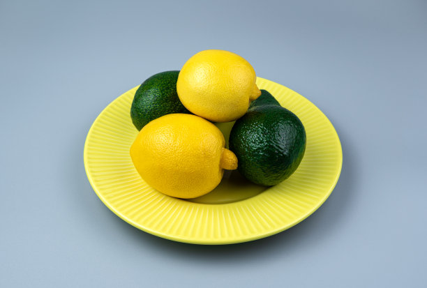 在灰色背景的黄色盘子里放上新鲜的柠檬和牛油果。有空间复制的侧视图图片下载