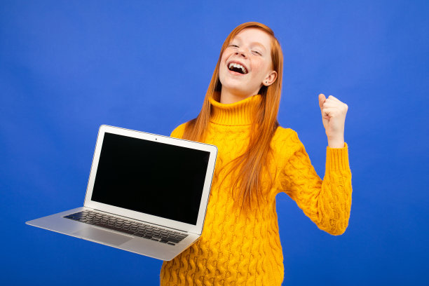 一个快乐的红发少年展示了一个笔记本电脑显示器，上面有一个蓝色演播室背景的广告布局图片下载