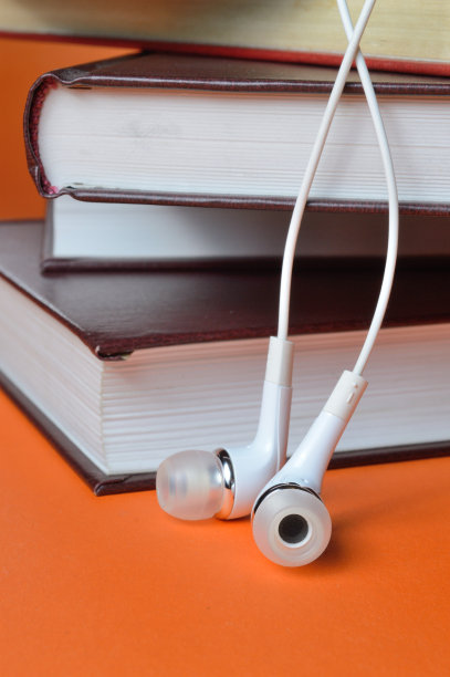 手机上的白色耳机放在橘黄色背景的一堆书上。图片下载