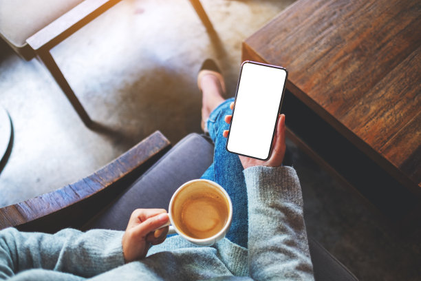 一个女人拿着手机和空白的桌面屏幕喝咖啡图片下载