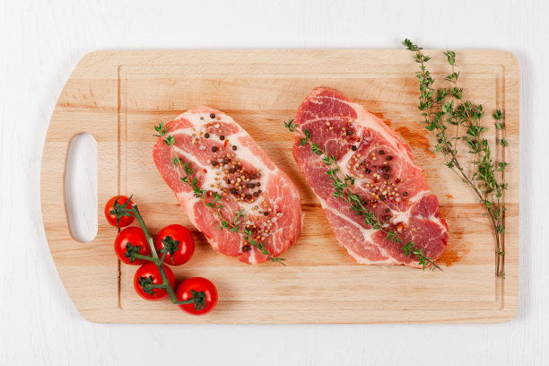 新鲜切好的生牛排，配上香料、西红柿和百里香，放在厨房的砧板上，放在白色的木桌上图片下载