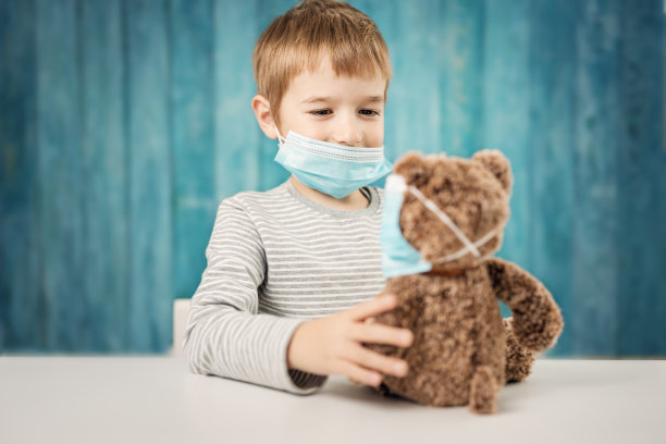 小男孩和泰迪熊戴着医用口罩坐在桌旁图片下载