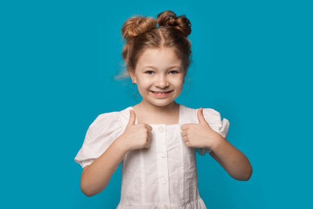 一个穿着白色连衣裙的可爱女孩正对着镜头微笑着，用手势在一面蓝色的墙上画着类似的标志图片下载