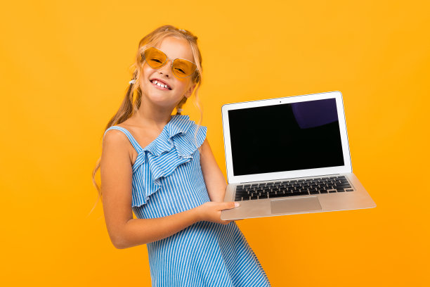 穿着衣服的快乐女孩微笑着，她的笔记本电脑被隔离在黄色和橙色的背景上图片下载