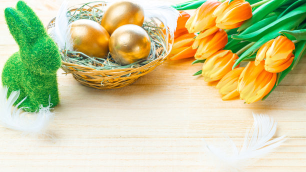 金色的复活节彩蛋在篮子里与春天的郁金香，白色的羽毛在木制的背景上装饰复活节快乐。春天节日的概念。图片下载